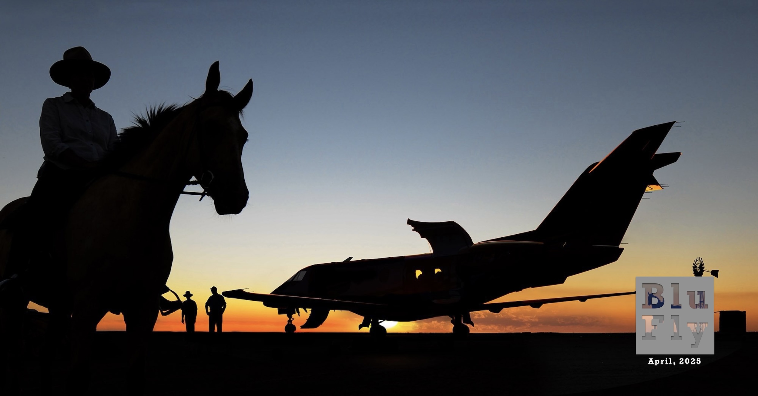 A silhouette of a Pilatus PC-24 executive jet is parked on what appears to be a flat farmer's field. The airstair is deployed at the front of the aircraft. A large cargo door is open at the rear of the aircraft. On the left side of the frame, there is a silhouette of a horse and rider quite close to the camera position. The rider is wearing a round cowboy hat. Between this element and the aircraft, in the distance, are silhouettes of two people who appear to be farmhands. To the right of the jet (although somewhat obscured by the BluFly logo, described below) is another silhouette of horse and rider at roughly the same distance as the farmhands. The horse and rider are immediately to the left of a silhouette of an agricultural rotary windmill, also at the same distance. To the immediate right of the windmill, and on the right side of the frame, is a small 'dog house' which may be connected to the windmill in some way. All these elements are backlit by a spectacular sunset or possibly sunrise. Superimposed on the bottom right corner of the photo is a grey, BluFly logo consisting of the words « Blu » on one line and then « Fly » on the next line. Both words are contained within a grey box. The former is shaded blue and the latter is shaded white. The logo letters are 'see through' such that elements of the photo can be seen through them. Below the logo are the words « April, 2025 » in a similar typeface in white. (📸 Jon Davison | Eye in the Sky Productions)