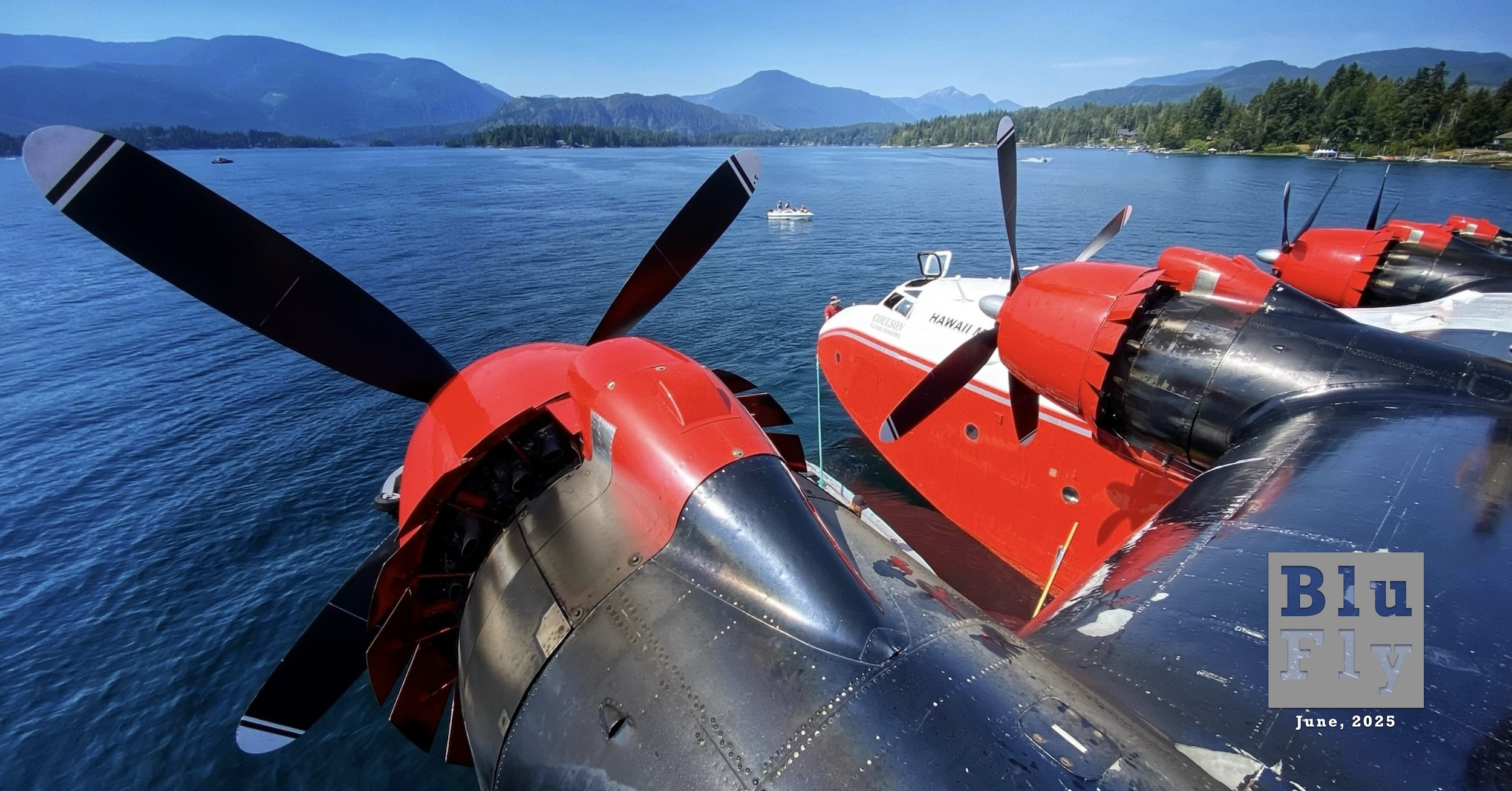 Coulson Aviation's 'Hawaii Mars' photographed while standing on top of the wing just outboard of the left-most engine. The camera is turned and oriented such that most of the leading edge and the aircraft's four engines are visible. The engines have four-bladed propellers. The nacelles and wing leading edge are painted black, with the exception of the forward part of each nacelle, just aft of the prop, which is painted red. The fuselage forward of the wing is also visible. Its lower surface is painted red matching the forward part of the nacelles. The upper surface of the fuselage is painted white. The partially obscured words « HAWAII MARS » are painted just aft of the cockpit, which is also visible. The aircraft is afloat on an expansive blue lake with tree-lined shores. The sky is completely clear and it's a sunny day. Original caption from source: « Dancing On Mars | Once in a lifetime opportunity to spend the morning with Captain Peter and the crew of Hawaii Mars before her historic final flight to her forever home at the British Columbia Aviation Museum. Shot August 8, 2024 at the Coulson Aviation Seaplane Base on Sproat Lake, British Columbia, Canada. » Superimposed on the bottom right corner of the photo is a grey, BluFly logo consisting of the words « Blu » on one line and then « Fly » on the next line. Both words are contained within a grey box. The former is shaded blue and the latter is shaded white. The logo letters are 'see through' such that elements of the photo can be seen through them. Below the logo are the words « June, 2025 » in a similar typeface in white. (📸 Cheryl Goodwin)