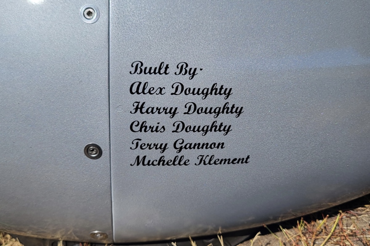 A grey wheel fairing from an RV-6 is pictured. In a script-like font, the following words appear: « Built By - ¶ Alex Doughty ¶ Harry Doughty ¶ Chris Doughty ¶ Terry Gannon ¶ Michelle Klement » The registration of the aircraft, not pictured, is « C-FYGI ». (📸 Alex Doughty)