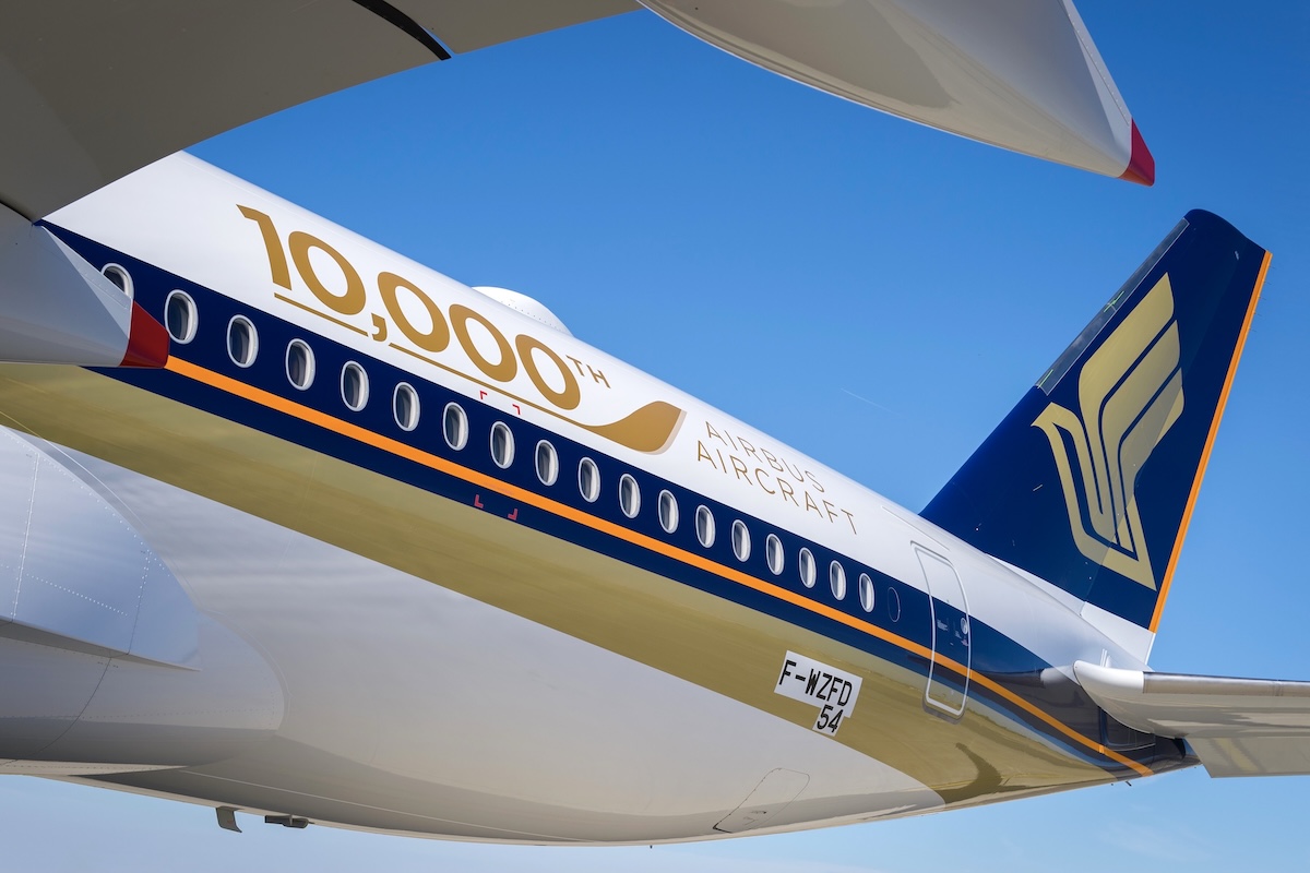 The tail of an Airbus A350-900 pictured while looking up and aft from from what seems to be just ahead ofm or under the wing. The aircraft is painted in Singapore Airlines livery and bears the registration number « F-WZFD ». The sky above is gin-clear blue. Painted above the passenger windows are the words « 10,000th AIRBUS AIRCRAFT ». A grey bar at the bottom of the photograph bears the copyright information on the left and the Airbus logo on the right. (📸 © AIRBUS S.A.S 2016 - photo by A. DOUMENJOU / master films)