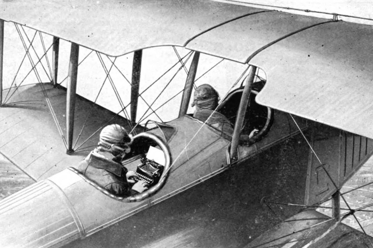 A vintage magazine advertisement with a photograph showing two people flying in an antique biplane. The person in the rear cockpit is using a typewriter.