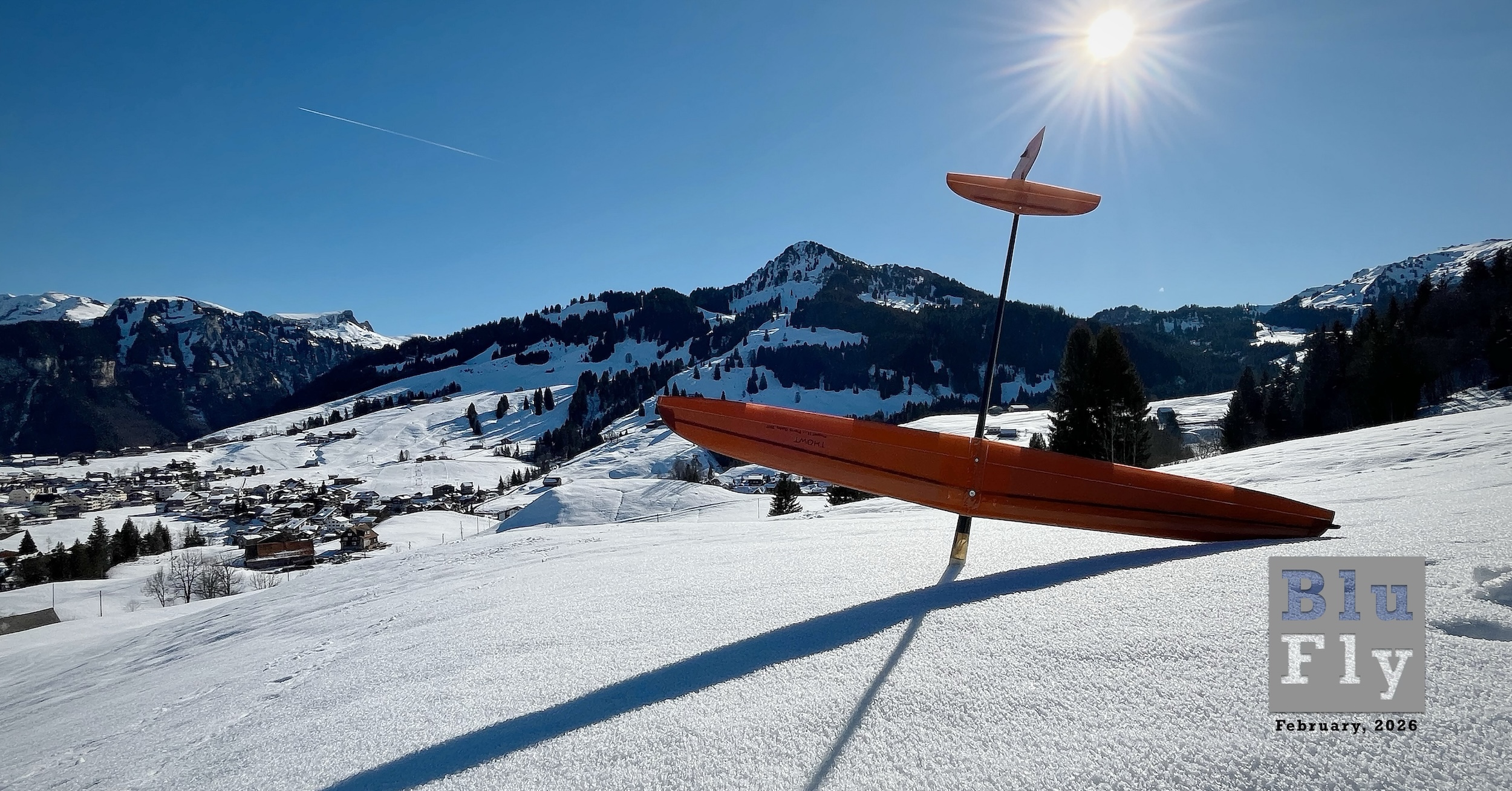 A model glider is nose down in a snowy field in the mountains. The sun shines, casting a shadow of the glider in the snow. (📸 ©2024 Pierre Gumy. All rights reserved. Used here with permission.)