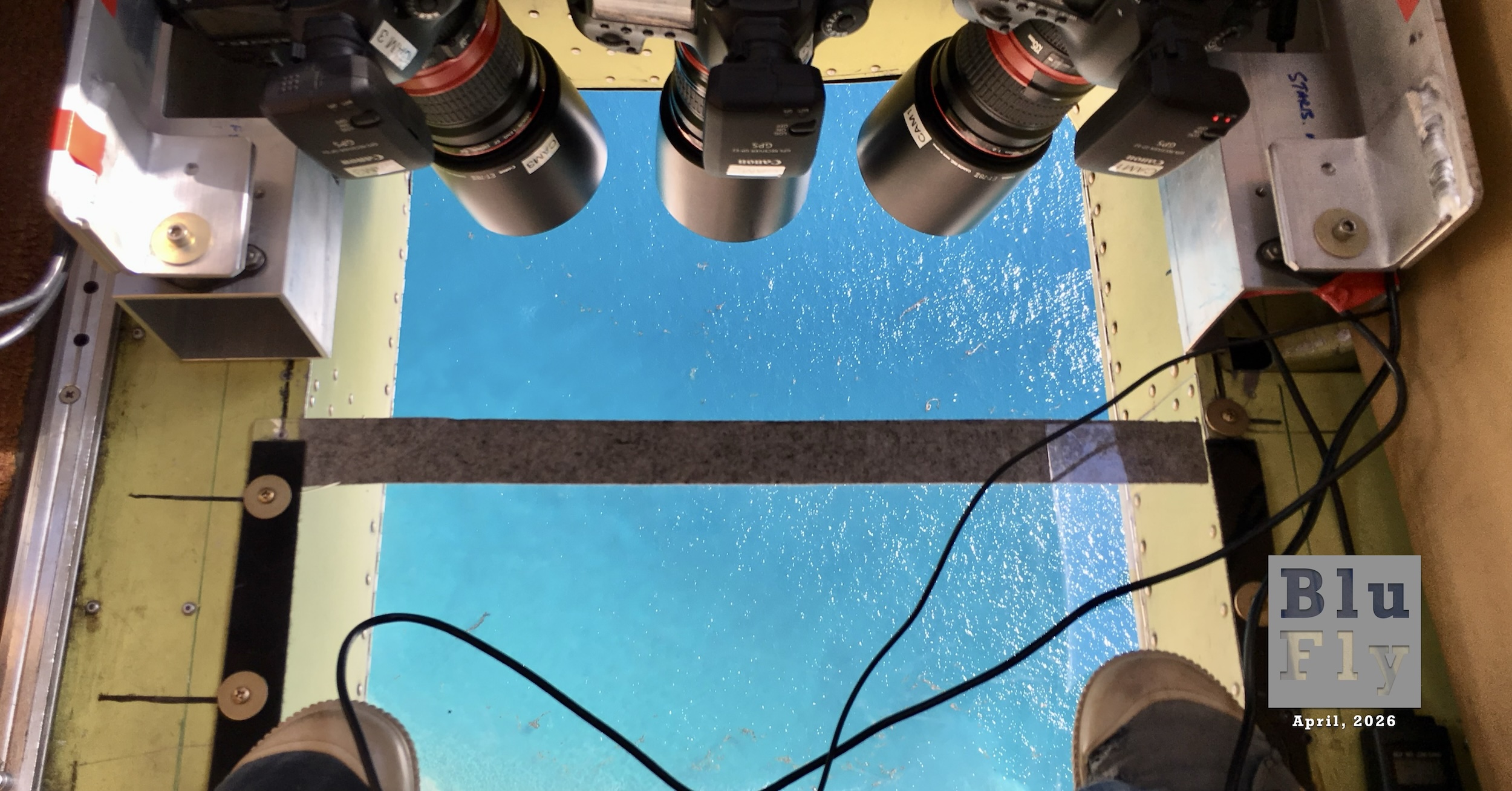 The view of a vivid blue ocean out the transparent belly port of an aircraft conducting a survey of marine wildlife. Whales are visible. (📸 Laura ‘Laney’ White, US Geological Survey in the public domain.)