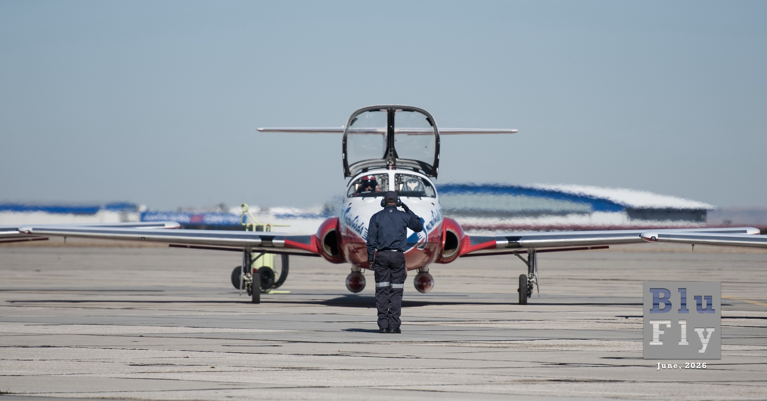 A RCAF CT-114 points directly at the camera. In front of it, a ground crew member with their back to the camera salutes the pilot.