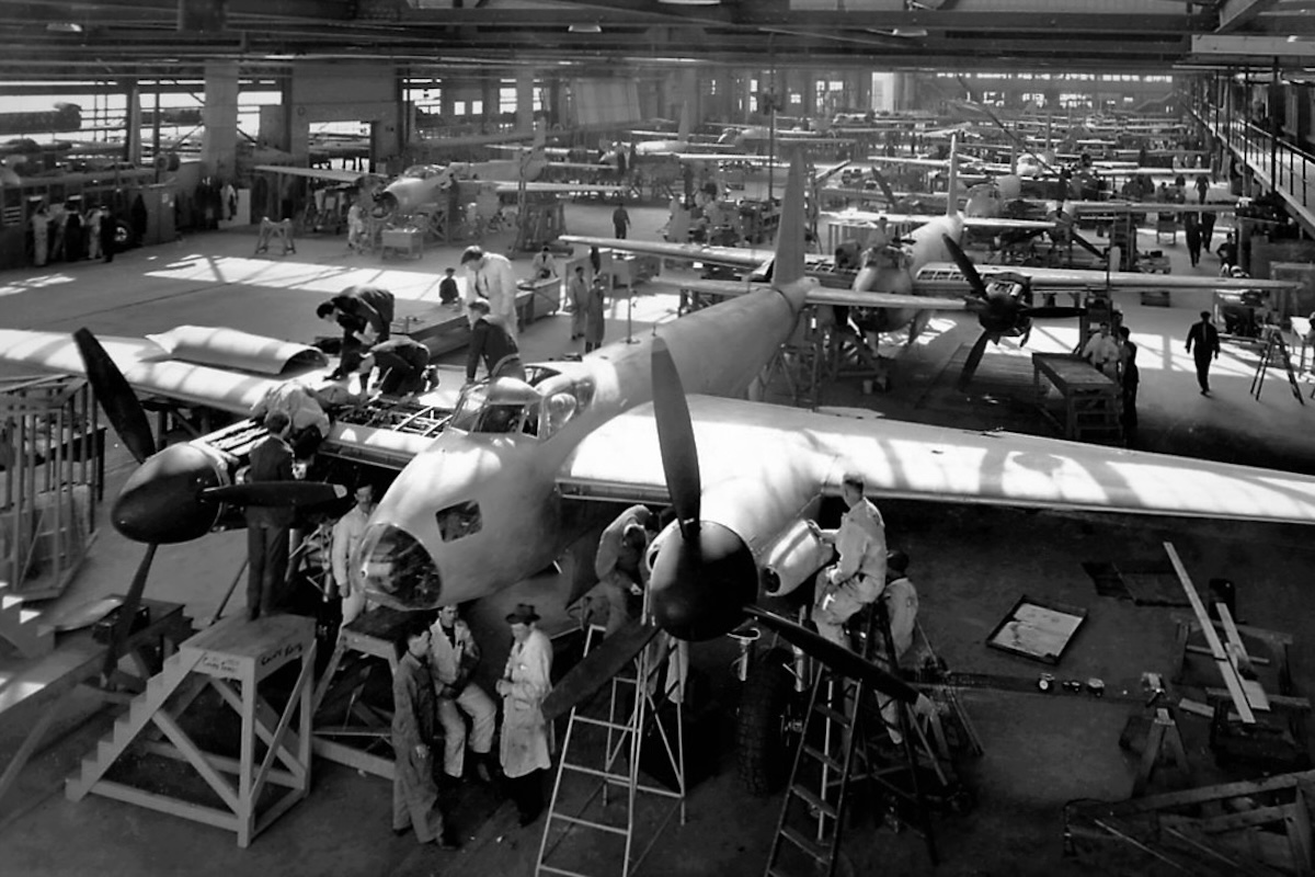 A black and white photo of De Havilland Mosquitos being built on an assembly line. They stretch as far as the eye can see.