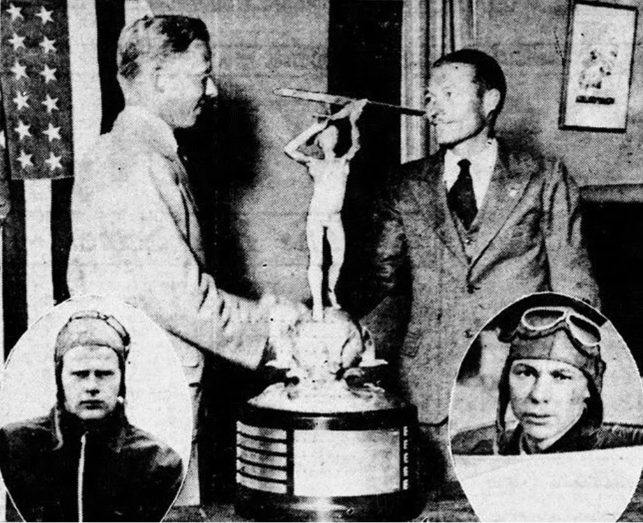 A grainy, vintage, black-and-white photo of a man, on the left, presented an ornate trophy to the man on the right. Both men are wearing suits and smiling as they shake hands. The trophy features a statue holding a small aircraft aloft in its hands, which, in turn, is mounted on a large, round base. A US flag, hanging in a vertical orientation, is partially visible on the left side of the frame. At the lower left and light right of the frame are oval, inset photos of two men wearing leather flying helmets. The connection between the inset photos and the main subjects of the photo is not clear. Original caption from source: « Primary glider instruction at Mines Field, Los Angeles with Hastings shown standing on the right. » (📸 Elmira Star-Gazette, October 6, 1930)