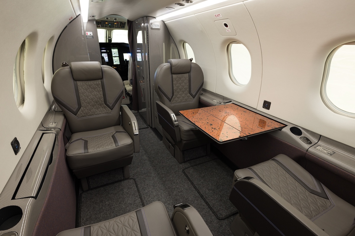 A Pilatus PC-12 interior. The pilots' cockpit is visible up front, with four club seats aft of this, separated with a brown conference table.