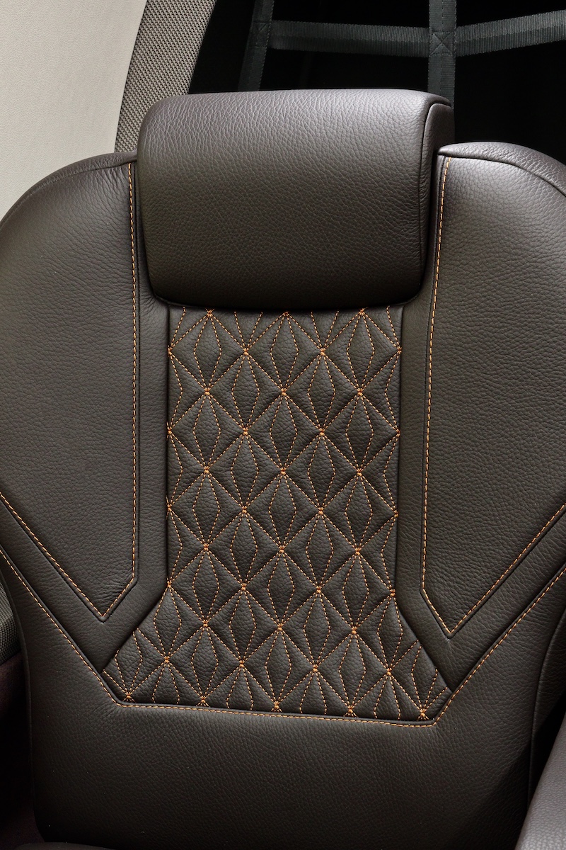 The dark brown leather seat and headrest of a Pilatus PC-12 interior. The seat features orange stitching in a diamond pattern.