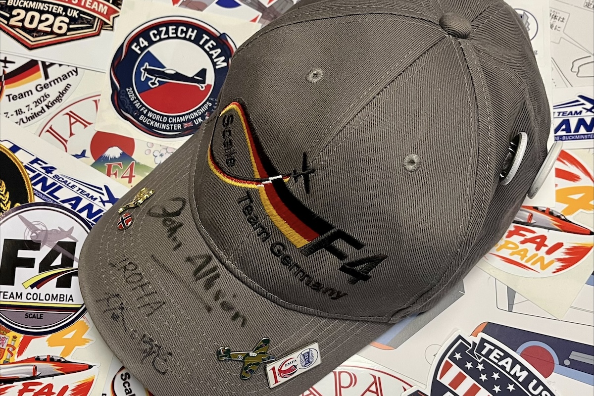 A hat stating 'Scale Team Germany' is sitting on a table festooned with many colourful stickers. There are pins and some writing on the brim.