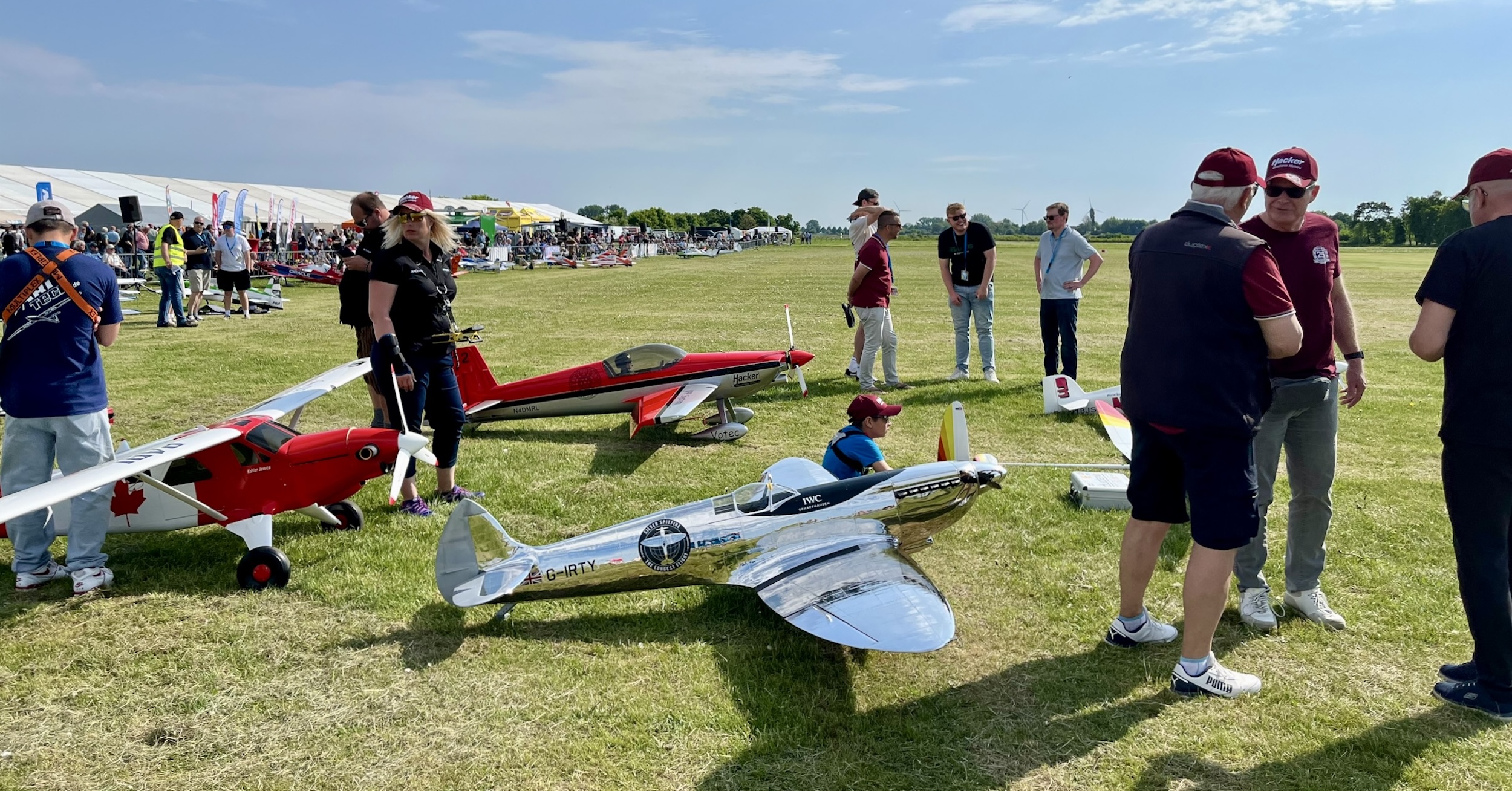 A boy sits beside a large, shiny silver Supermarine Spitfire model while participating in a competition for such models. Other participants and spectators surround them.