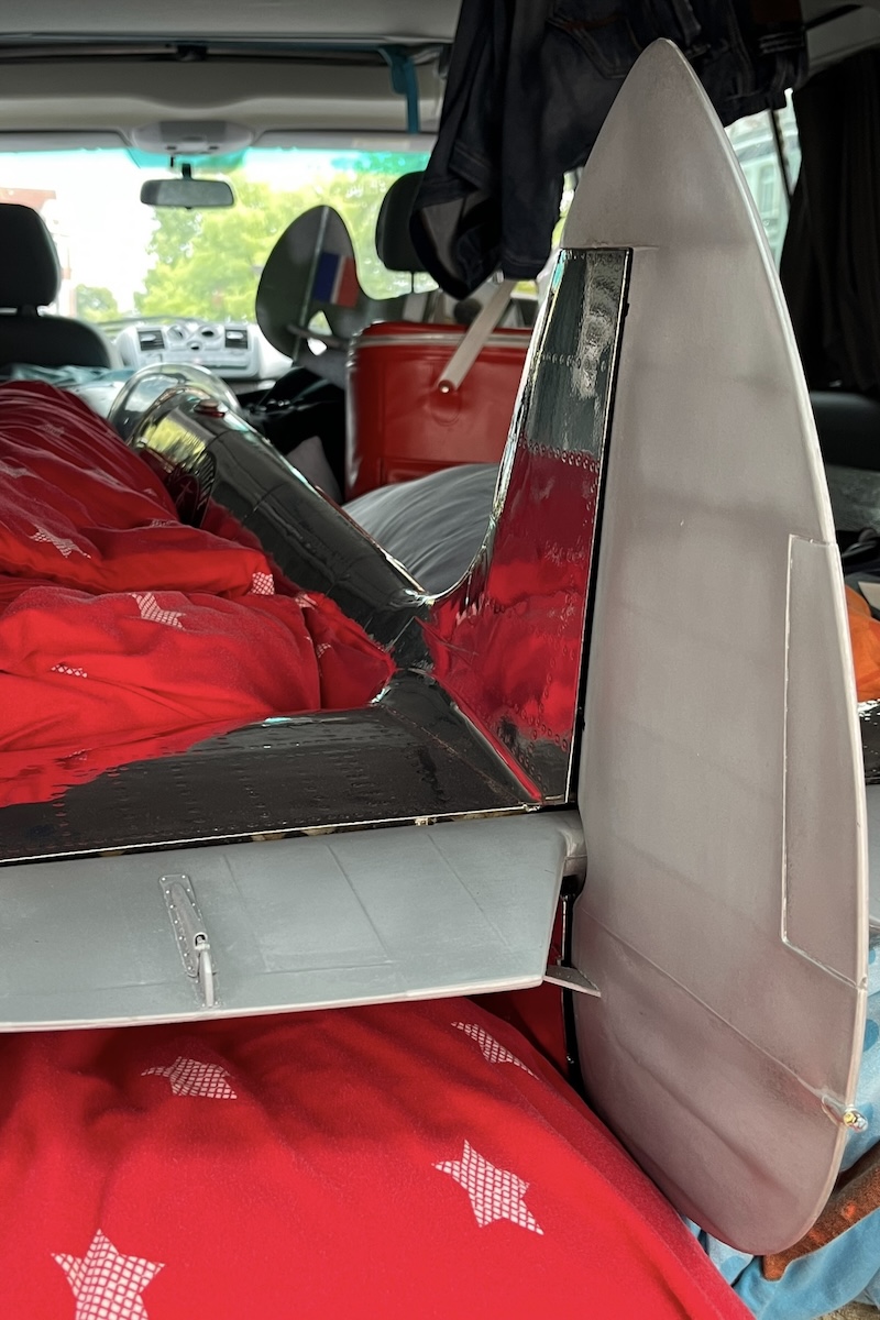 The fuselage of a model aircraft loaded into a hatchback-type car. It is surrounded by other luggage such that the fuselage is unlikely to move. 