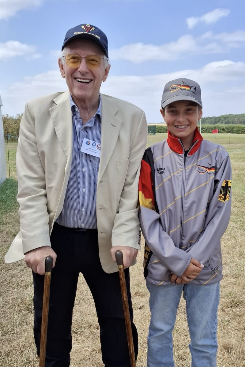 An older, grey-haired man, on the left and holding canes in both hands, and a boy on the right stand and smile for the photo.