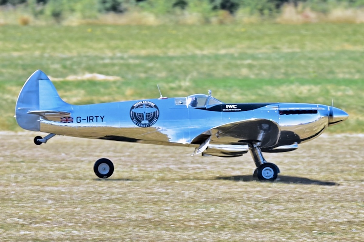 A model of a Supermarine Spitfire, in a chrome-like finish, is captured while landing. One wheel has come off and rolls along behind the aircraft. 