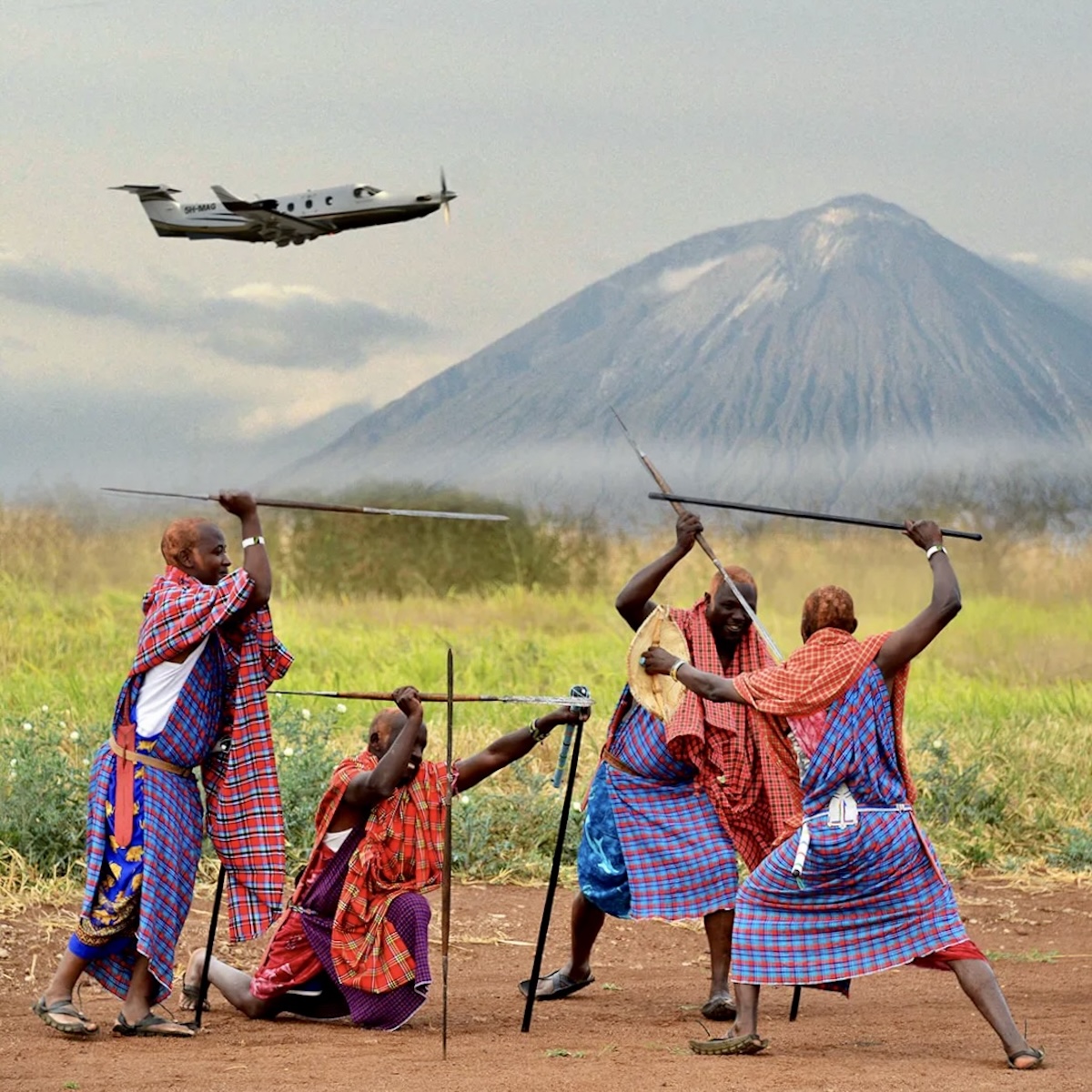 A group of four Maasai tribemen wearing their traditional shúkà are carrying their distinctive spears and are pictured engaged in mock combat. In the background, the Pilatus PC-12 rises from the landscape and climbs out. The aircraft is flight from left to right in the frame. In the far distance, Mount Ol’Doinyo rises above the grassy plain. (📸 ©2017 Jon Davison | Eye in the Sky Productions) (📸 ©2017 Jon Davison | Eye in the Sky Productions)