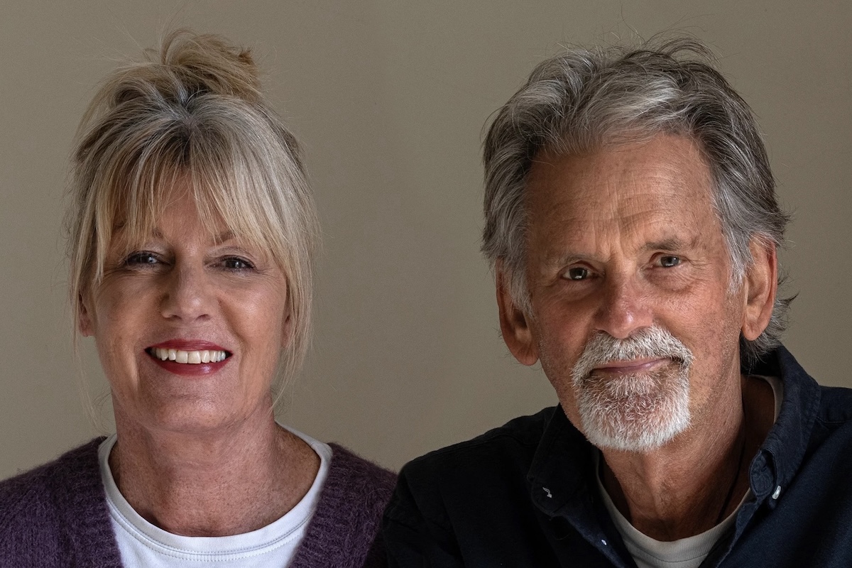 An attractive, older couple look directly at the camera in a studio-quality portrait. On the left, she has blonde hair; he has grey.