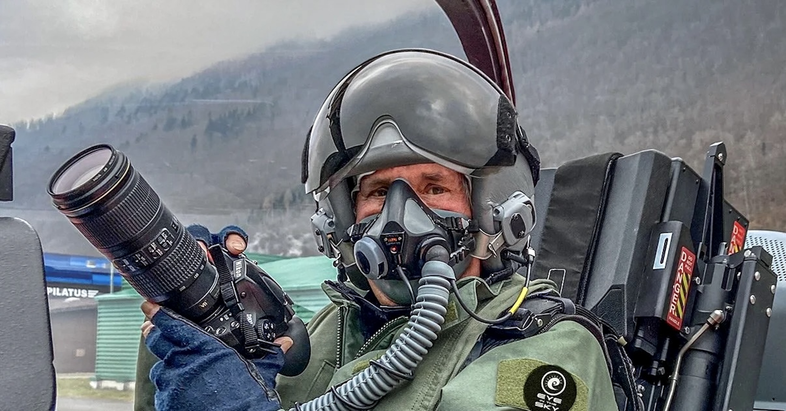 A man in a flight suit and helmet in the rear seat of a Pilatus PC-21, with the canopy open. Only his eyes are visible.